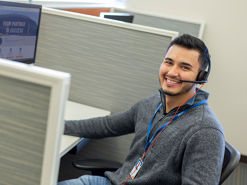 Employee in cubicle wearing headset and grey shirt smiling