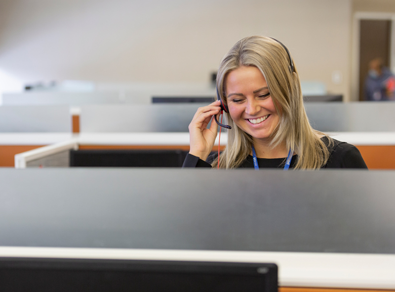 Employee in cubicle wearing headset and grey shirt smiling