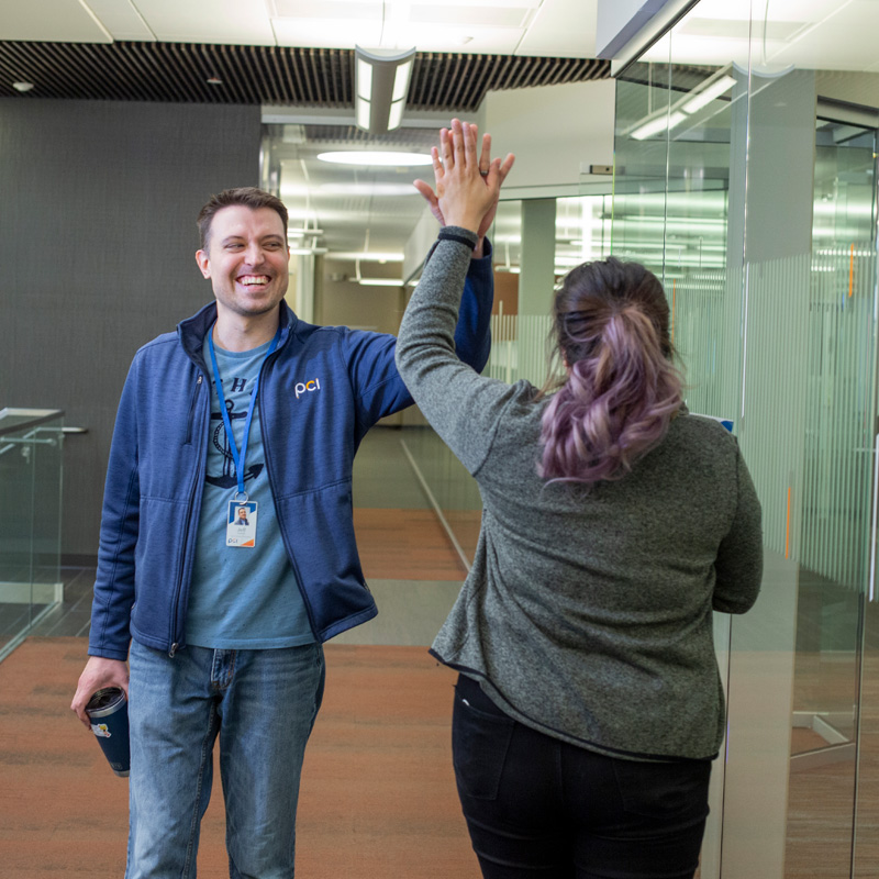 PCI employees walking in office hallway and giving a high five